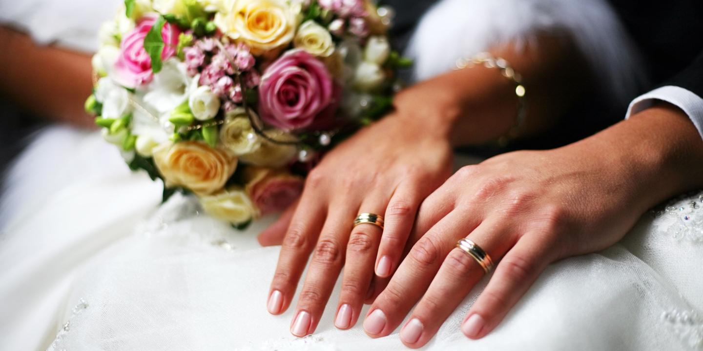 Wedded couple's hands with rings and floral bouquet